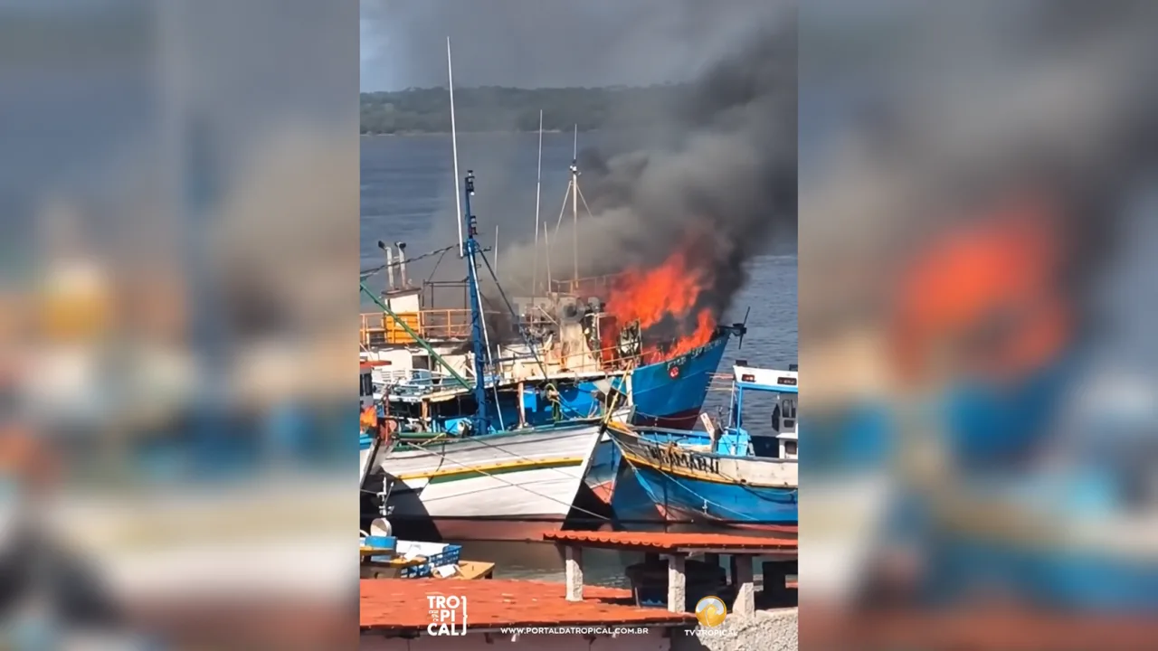 Embarcação em chamas no Rio Potengi, em Natal, com intensa fumaça escura visível entre outros barcos atracados