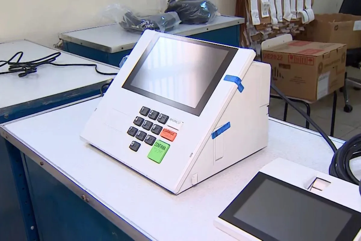 Equipamento eletrônico de votação sendo manuseado pela equipe técnica após incidente.