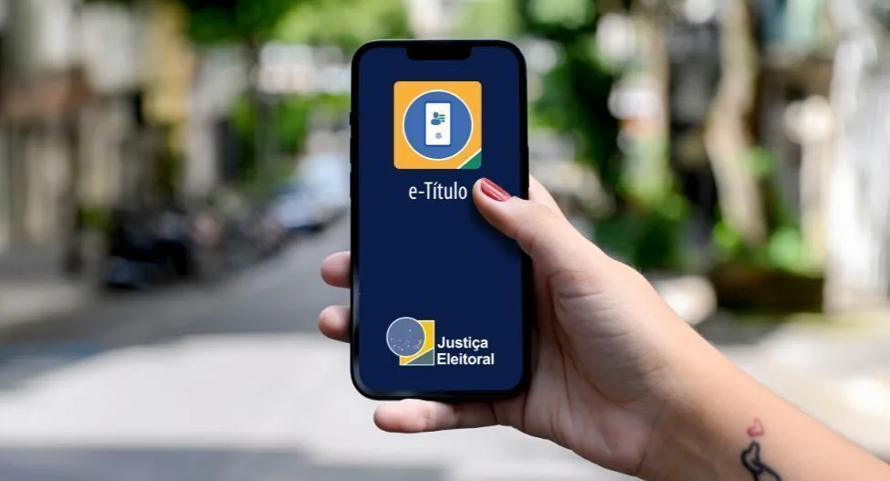 Mão segurando celular com a tela do aplicativo e-Título aberto durante o dia de votação.