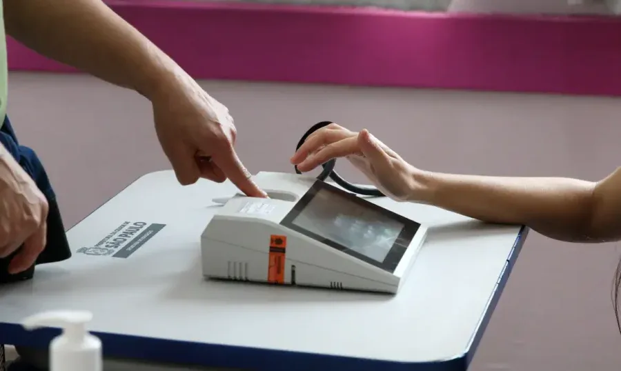 Urna eletrônica com leitor biométrico em seção eleitoral.