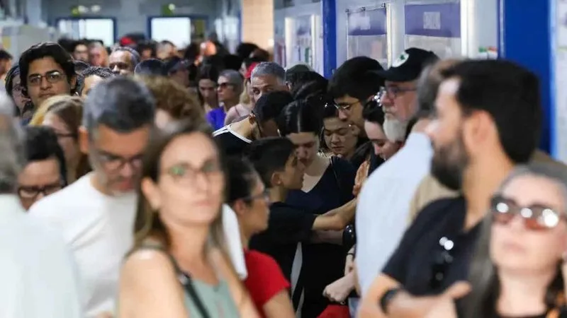 Urna eletrônica em uma seção eleitoral com eleitor ao fundo.