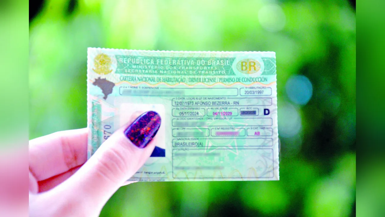 Mão segura uma Carteira Nacional de Habilitação.