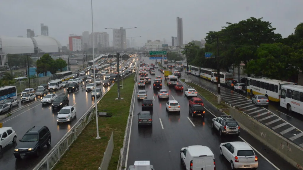Trânsito em Natal sob chuva, com fluxo intenso de veículos na BR.