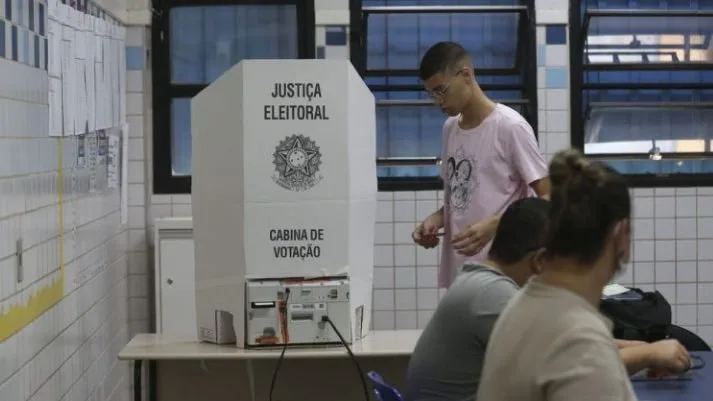 Mãos segurando um celular com o aplicativo e-Título aberto para consulta eleitoral.