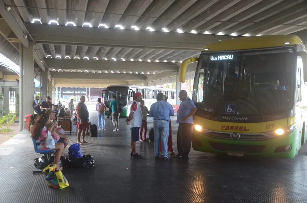 Ônibus intermunicipais estacionados no Terminal Rodoviário de Natal, com passageiros aguardando embarque e conversando na plataforma