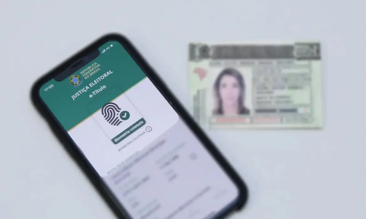 Eleitor segurando um título de eleitor com foco na tela de um celular.